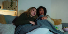 Two smiling women watch TV at home in the evening with dim lighting