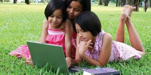 Three children laying on the grass looking at a laptop