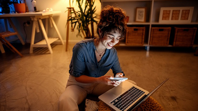 Woman using laptop and phone in living room at night