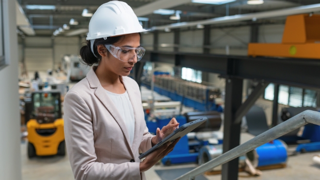Woman working in an industrial facility Woman at an industrial facility wearing a white safety helmet, safety glasses while working on a tablet device.