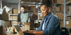Two people working in a warehouse filled with cardboard boxes.